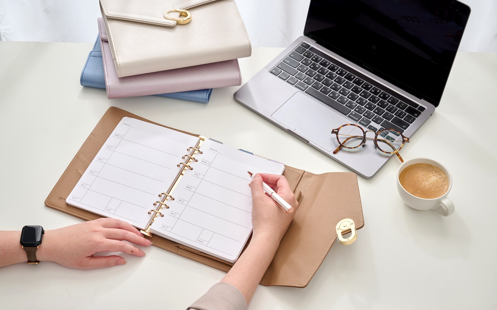 Writing meeting follow-ups in an EGOSUNNY planner beside a laptop