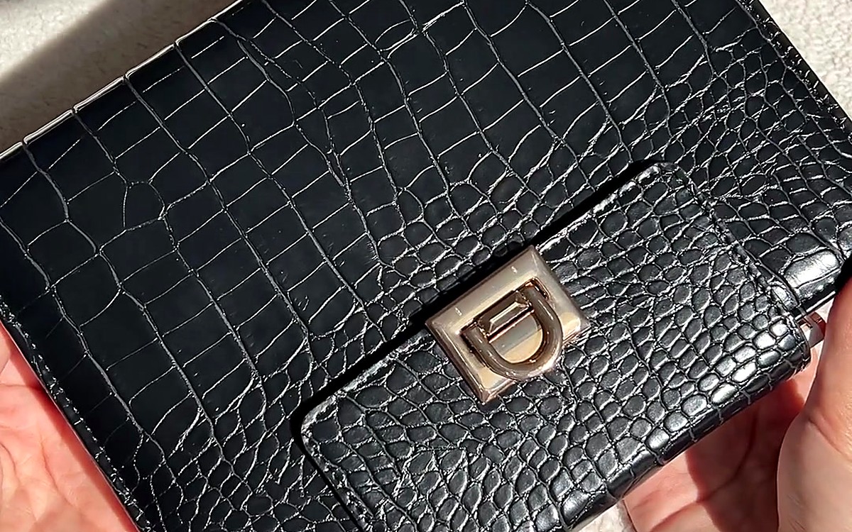 Hands holding a black textured EGOSUNNY clutch planner with a gold clasp