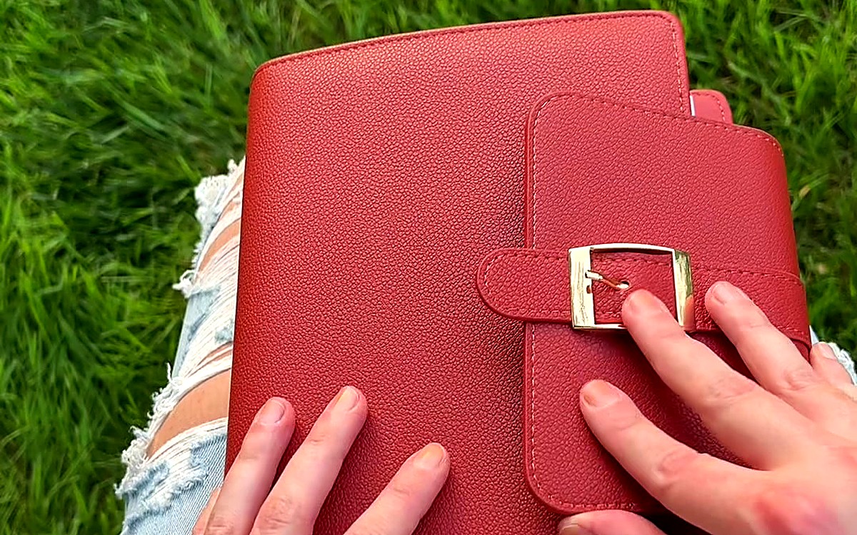 Hands holding a red EGOSUNNY Belt planner with its buckle closure outdoors