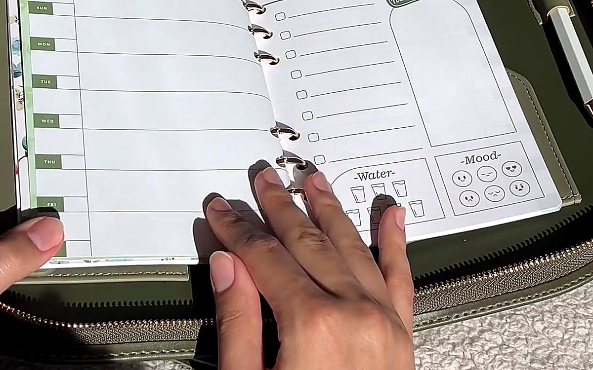 Hands holding open a green EGOSUNNY planner with rings and pages visible