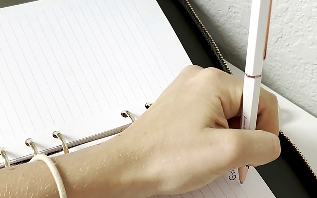 Hand with a white pen over a clean page in a ring-bound planner