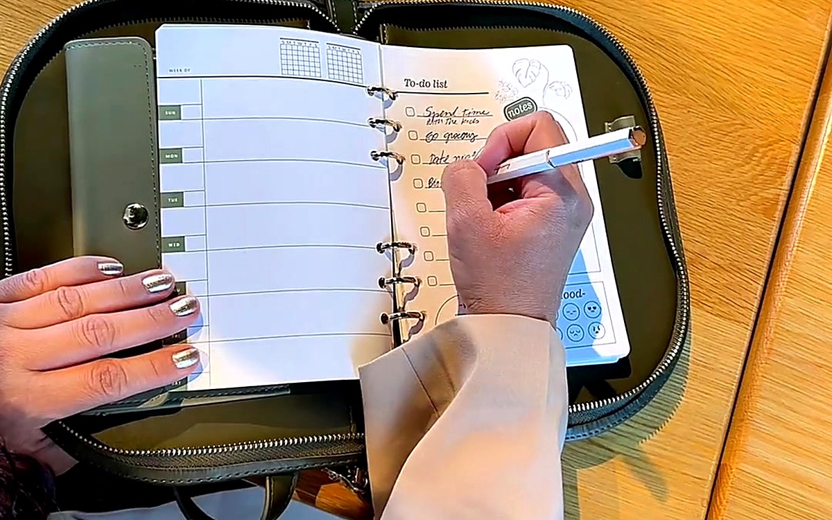 Hands writing a to-do list inside a green EGOSUNNY planner on a wooden table