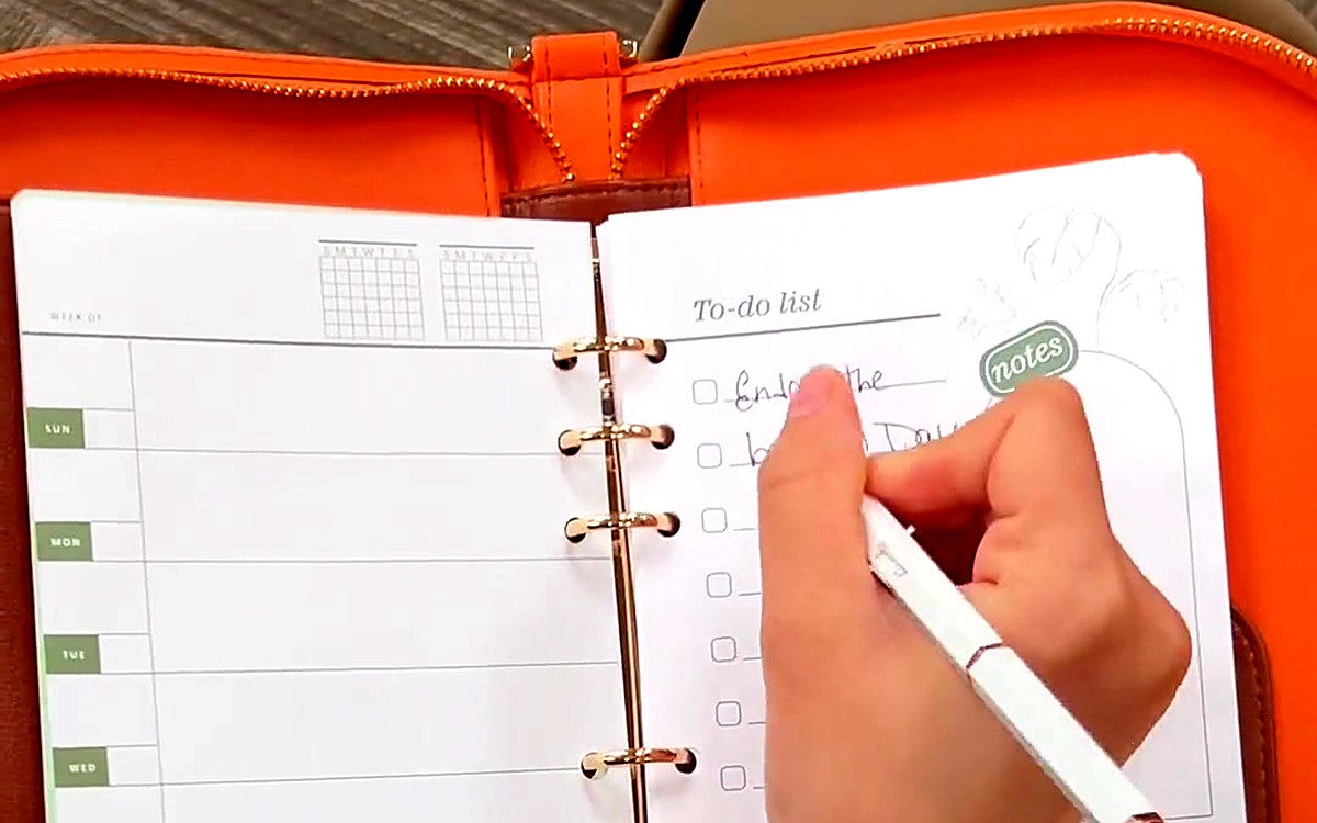 Hand writing a to-do list inside an orange EGOSUNNY planner
