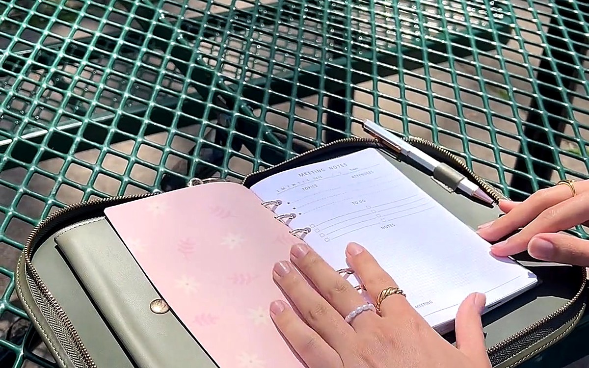 Hands opening an olive EGOSUNNY planner on an outdoor mesh table