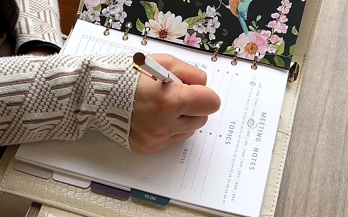 Hand writing meeting notes in a floral-bordered planner