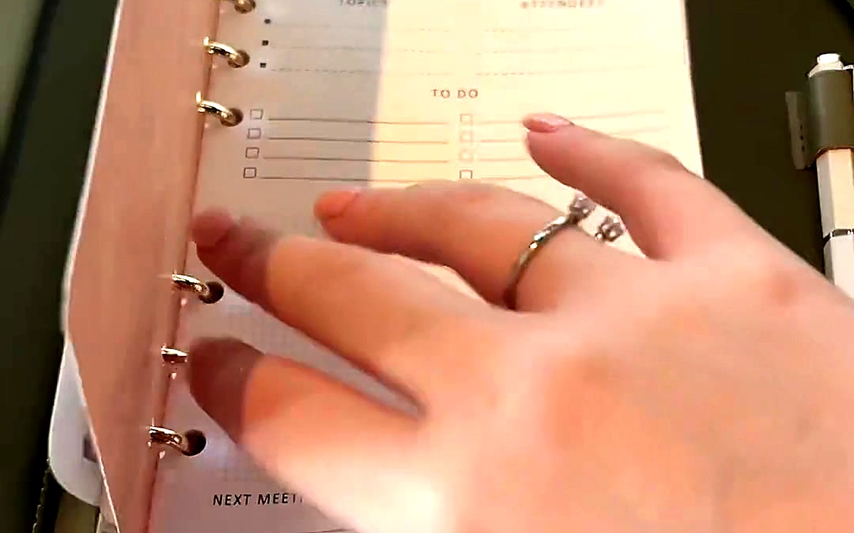 Hand turning a to-do page inside a rose-gold ring planner