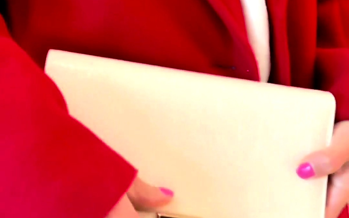 Hands holding a cream EGOSUNNY clutch planner against a red blazer