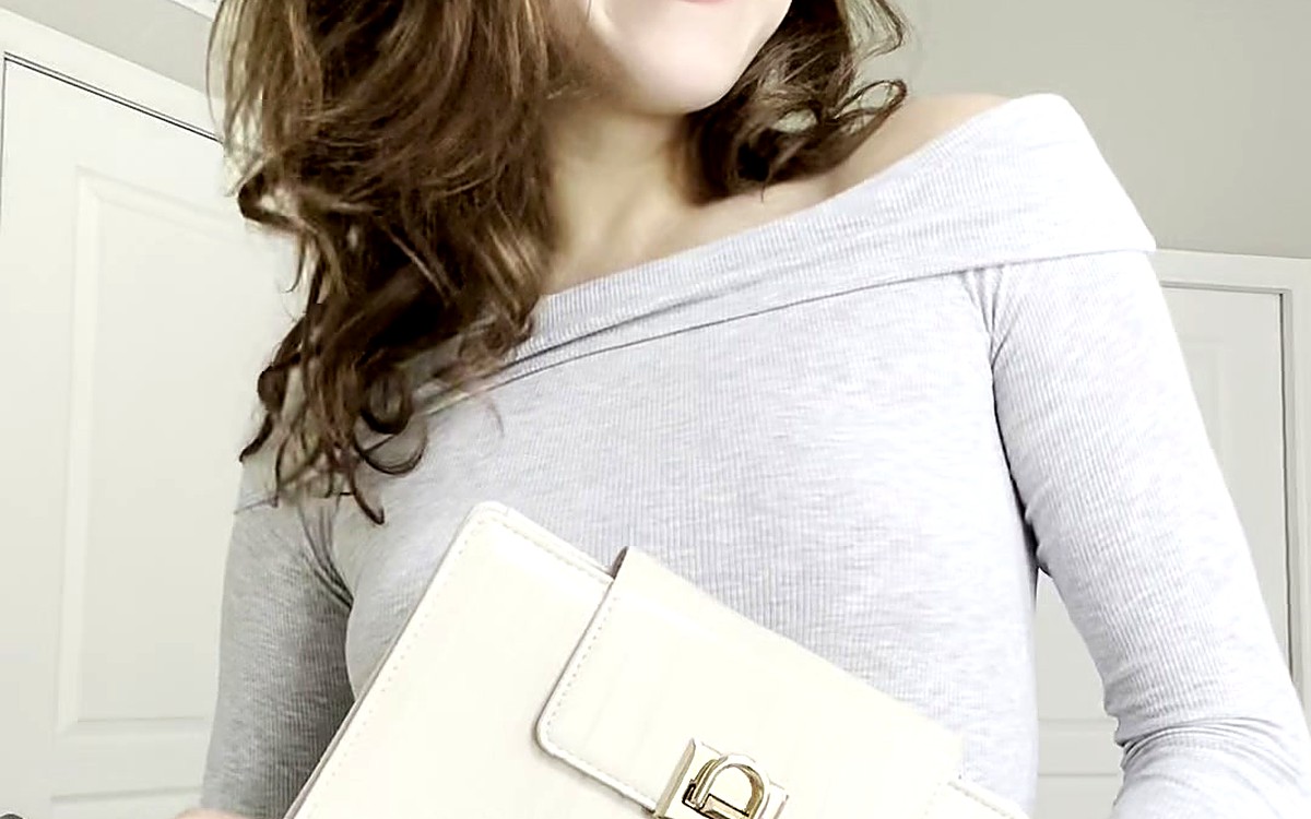 Woman in a gray top carrying a cream EGOSUNNY piece with a gold clasp