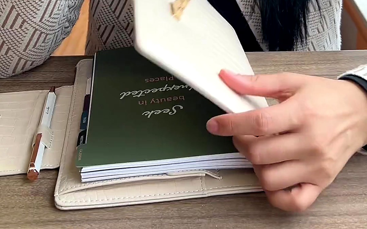 Hand opening a cream EGOSUNNY planner beside a coffee cup
