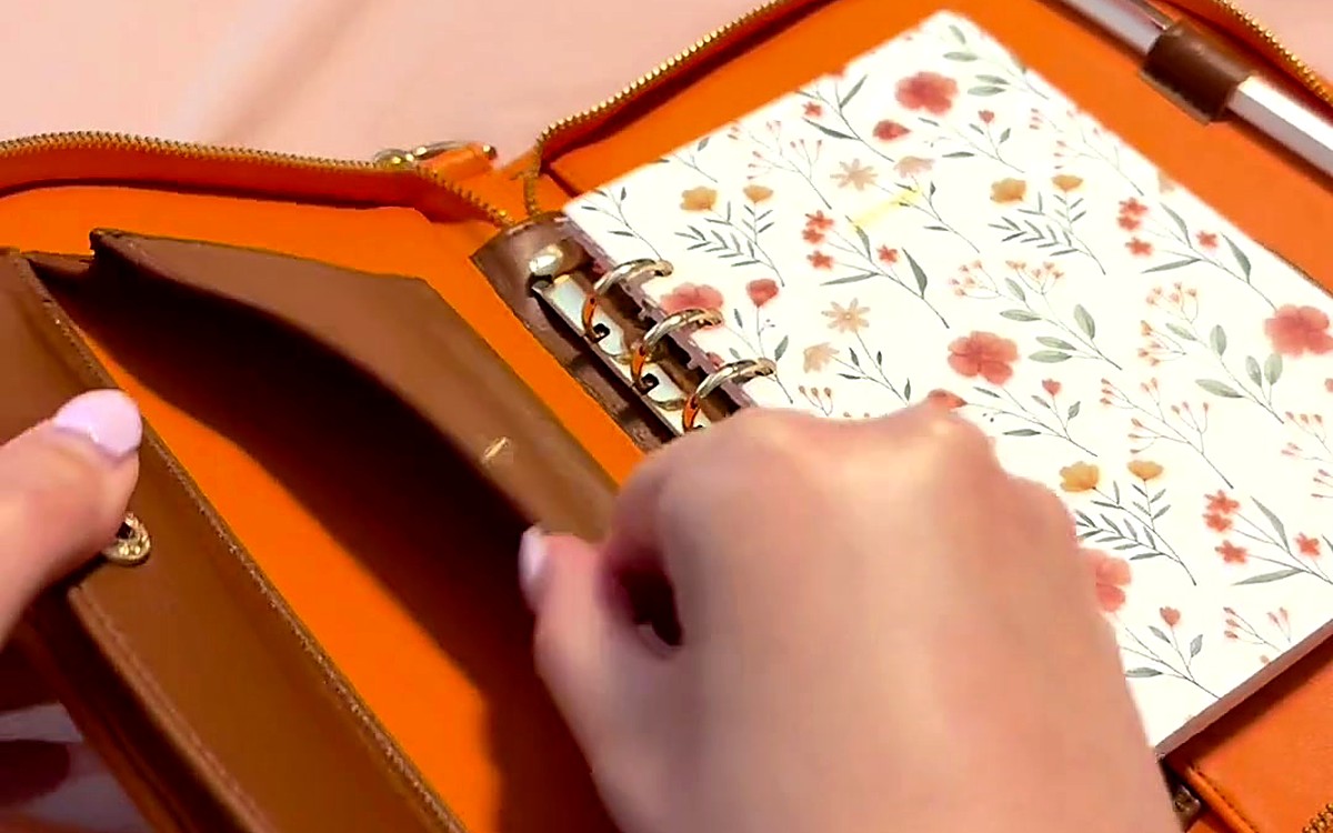 Hands opening a tan zippered EGOSUNNY planner with a floral insert