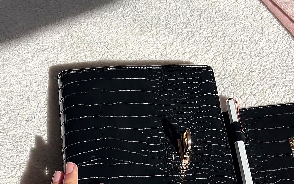 Black textured EGOSUNNY binder with a gold clasp in sunlight
