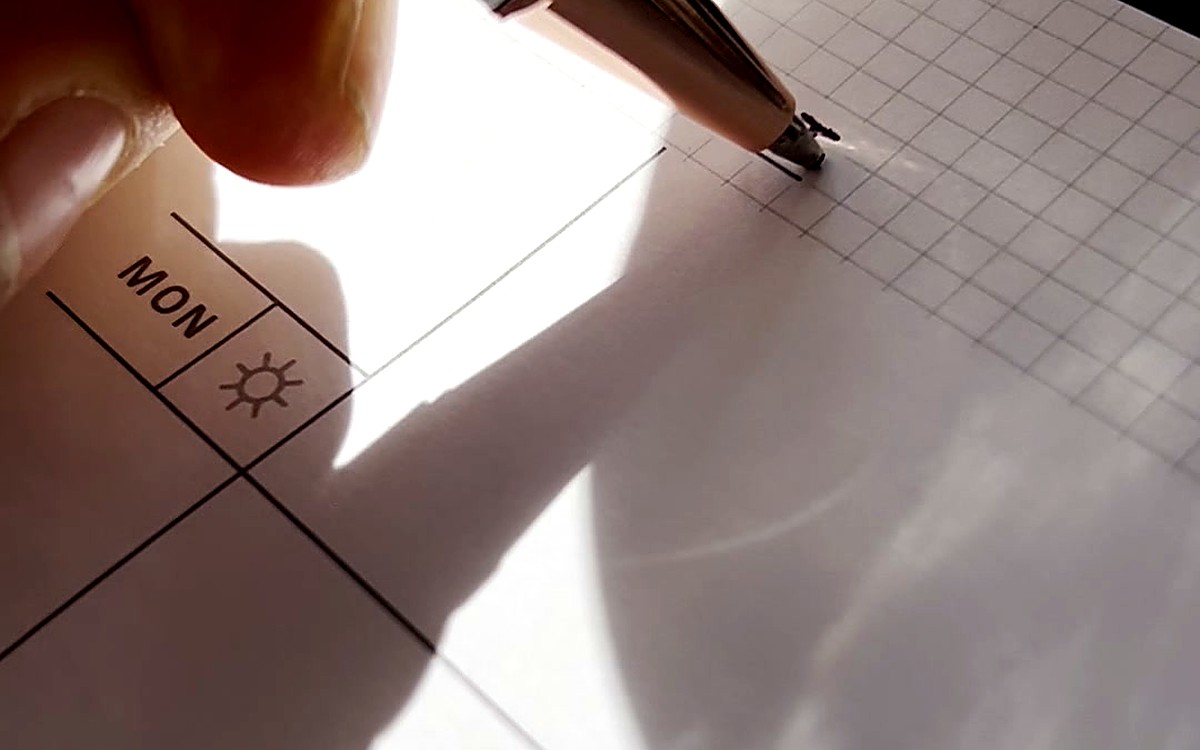 Hand pointing at a weekly grid in bright sunlight
