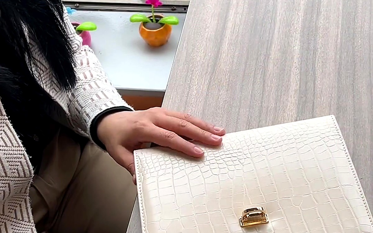 Hand resting on a cream textured EGOSUNNY clutch on a wooden desk
