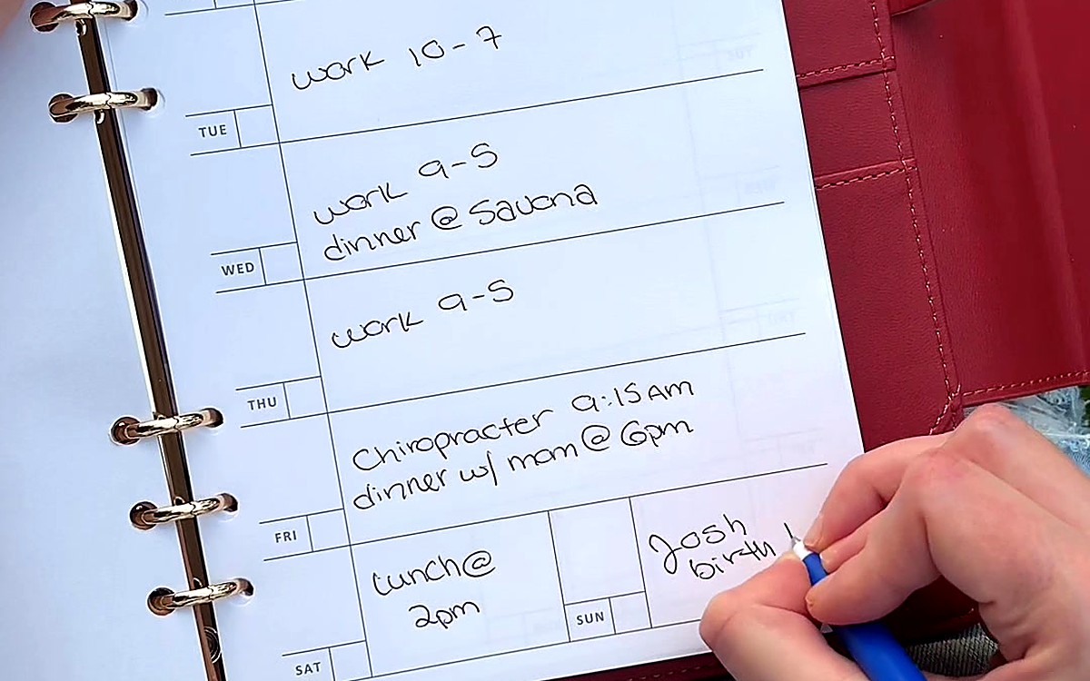 Hand writing a weekly schedule in a red EGOSUNNY Belt planner