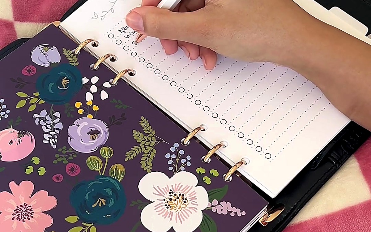 Hand writing beside a floral divider in a ring-bound planner