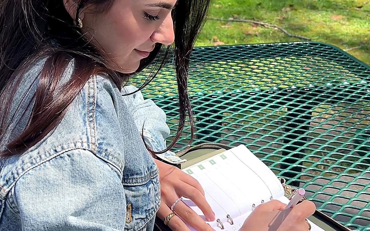 Woman writing in an open planner at an outdoor table
