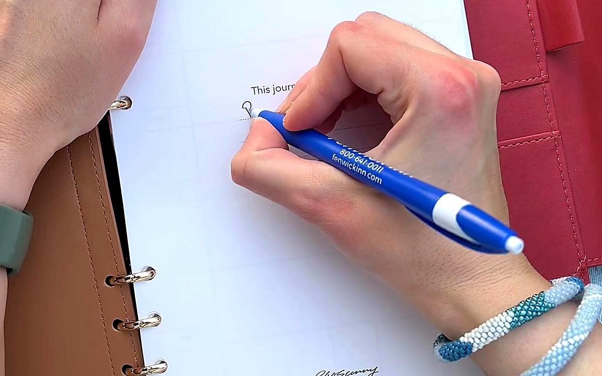 Hand writing a list on a lined planner page with a blue pen