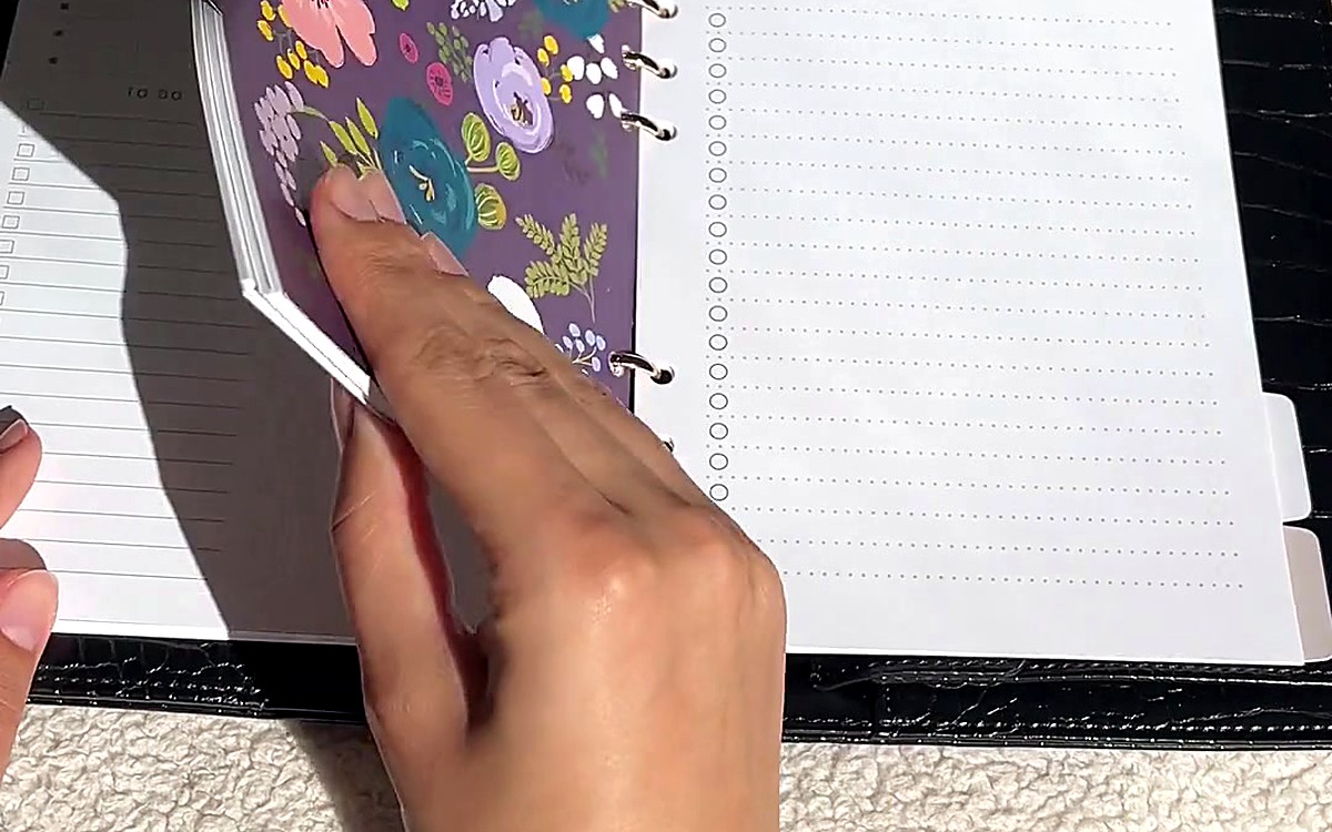 Hand turning a floral card inside an open black planner