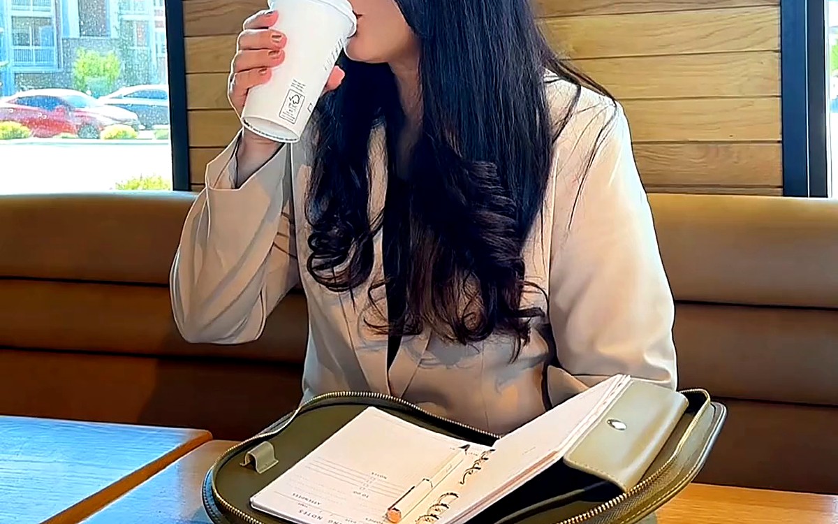 Woman with a drink and an open planner at a café table