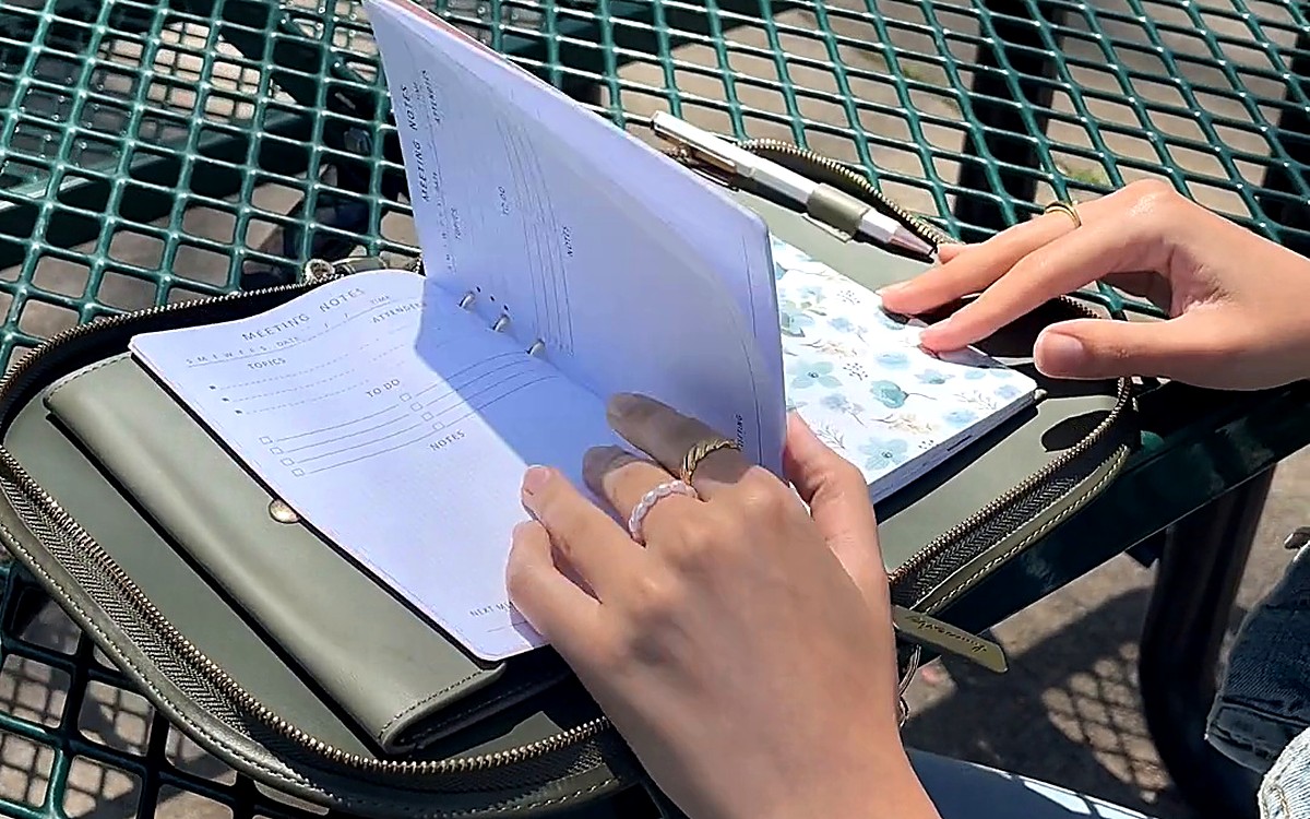Person writing in a planner at an outdoor table